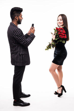 Indian man taking photo of his girlfriend with bouquet of red roses on the phone on white backgroundの写真素材
