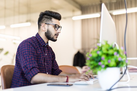 Happy young businessman sitting at his desk with laptop