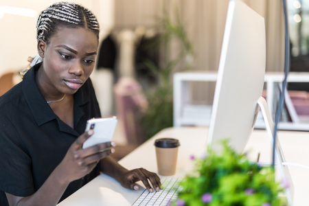 An African American businesswoman uses her mobile phone at her deskの写真素材