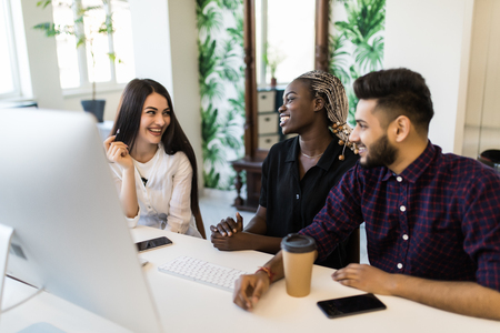 Focus on positive caucasian confident team leader mentor use computer sitting together with diverse female colleagues at desk helping explaining to new employees corporate program giving instructions.