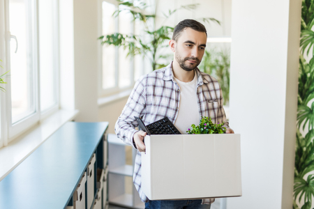 business, firing and job loss concept - fired male office worker with box of his personal stuff and his sad colleagues