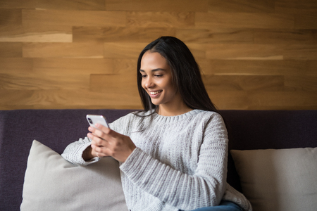 Pretty young woman lying on the couch and texting with her smartphoneの写真素材