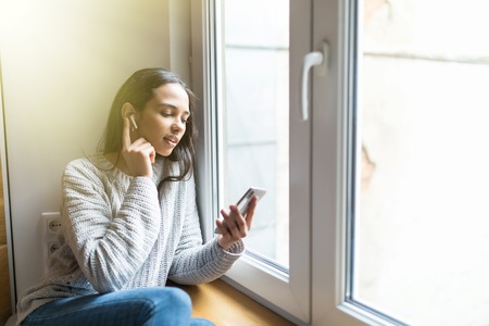 Woman listening music in headphones on windowsill backgroundの写真素材