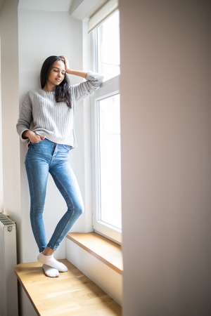 Portrait of young pretty woman standing at window in bedroom, drinking coffee and looking outside enjoys of restの写真素材