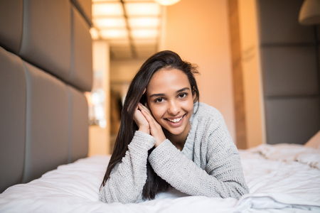 Natural beauty. Young woman looking at camera and smiling while lying on the bed at homeの写真素材