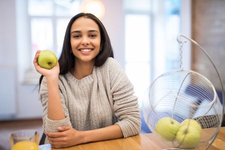 Happy young woman eating apples on kitchenの写真素材