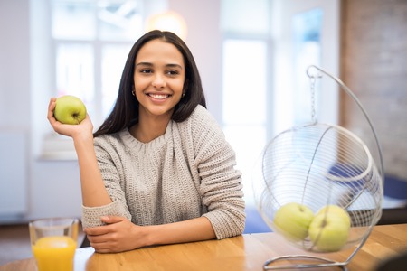 Happy young woman eating apples on kitchenの写真素材