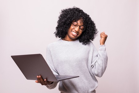 Portrait of a happy african woman using laptop computer make winner gesture posing isolated over white backgroundの写真素材