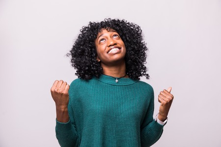 Portrait of a happy young african woman celebrating success isolated over beige backgroundの写真素材