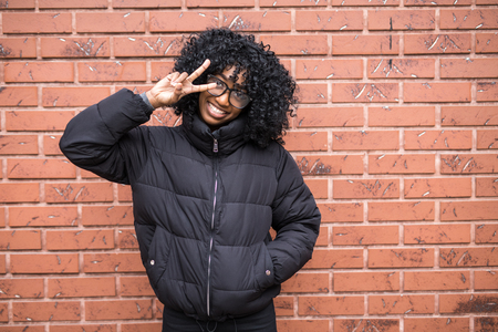 Portrait of young curly african woman standing in front of brick wall.の写真素材