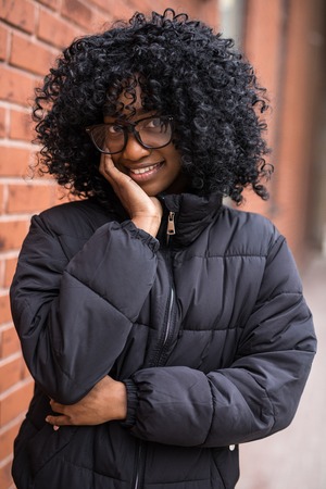 Portrait of young curly african woman standing in front of brick wall.の写真素材