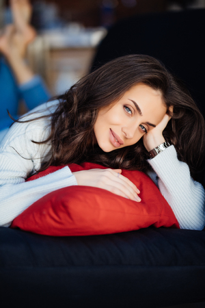 A woman looking at the camera is lying on a couch resting her head on a pillowの写真素材