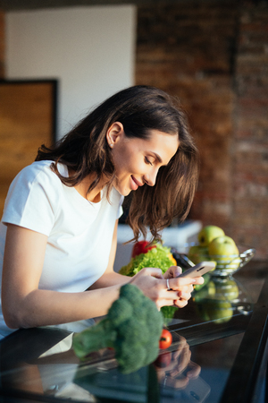 Portrait of her she nice-looking attractive lovely girl reading recipe online on the phone fresh lunch dinner farm organic vegs in light white interior room.の写真素材
