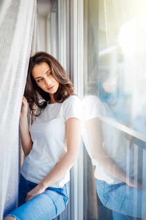 Beautiful woman in white standing near windowの写真素材