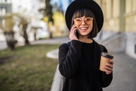 Young woman stands near office centre with cup of coffee and talks on smart phone. Business...