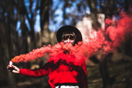 Young woman holding red colorful smoke bomb on the outdoor park.Red smoke spreading in the cerebration festival.の写真素材