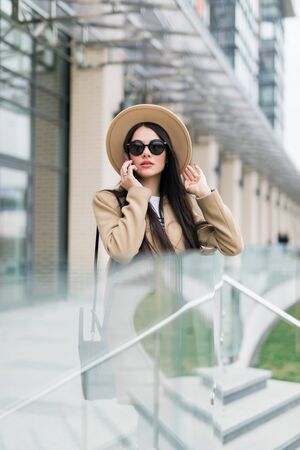 Caucasian business woman speaking by phone. Waist up portrait of a successful European business woman woman, talking on the phone, standing on glass background, modern office building.の写真素材