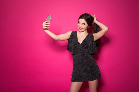 Studio portrait of woman smiling with white teeth and taking selfie isolated over pink background