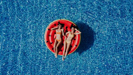 Aerial view of two women floating on inflatable mattresses relaxing in the swimming pool