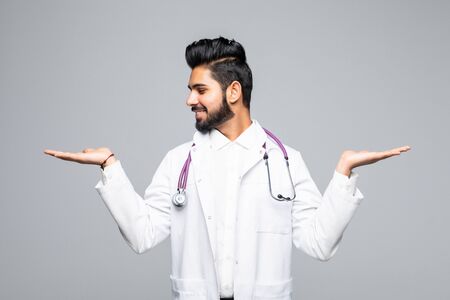Smiling indian male doctor holding palms upwards as copyspace on white backgroundの写真素材