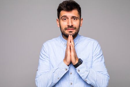 Picture of young guy dressed casually isolated on grey background, having put hands together in...