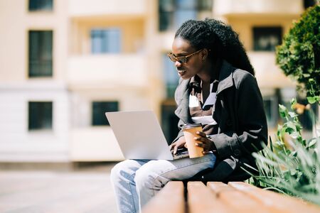 Portrait of African American girl sitting on bench and drinking coffeeの写真素材
