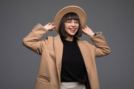 Fashion portrait pretty woman wearing beige coat and hat over grey background