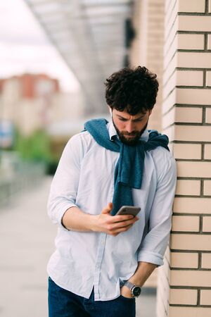 Portrait of man typing on his phone in the street. Outdoors.の写真素材