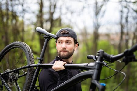 Happy handsome biker holding bike in the natureの写真素材