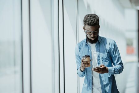 Young Afro American man standing in modern business building smiling and use phoneの写真素材
