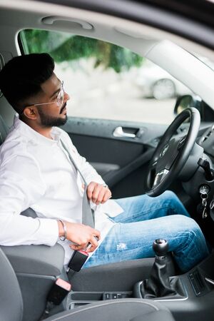 Portrait of handsome young man sitting in driving seat of car and wearing seatbelt for safetyの写真素材