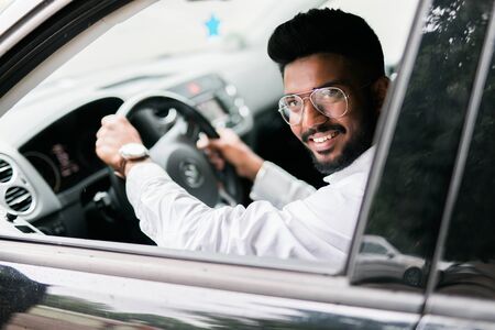 Closeup portrait, young handsome man in his new silver gray car, relaxing, hand on steering wheel,...