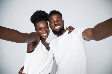 Couple selfie. Studio shot of casual african-american couple grimacing and showing victory sign on white studio background, copy space, isolatedの写真素材