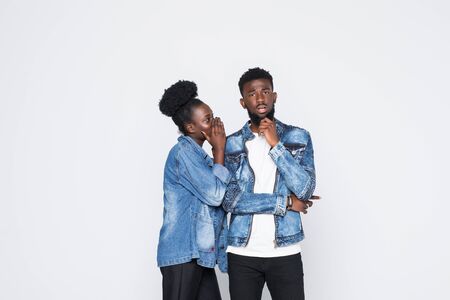 Secret, gossip concept. Young woman whispering a secret behind her hand to afro man. African couple isolated on trendy gray studio background.の写真素材