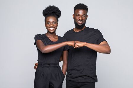 Beautiful young African woman hugging her boyfriend and looking at camera while standing isolated on whiteの写真素材