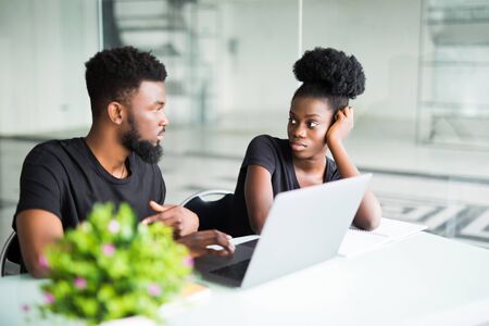 Portrait of two colleagues working together at a cafe, discussing business ideas and plans, using laptop computer: African man holding a pen, pointing at the screen while presenting his projectの写真素材