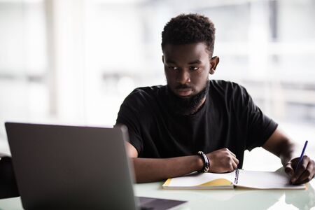 Image of young African man looking at camera with laptop near byの写真素材