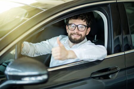 Dream came true. Cheerful casual guy smiling happily showing thumbs up sitting in a big white car