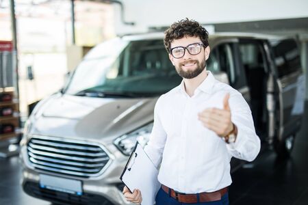 Confident young car dealer standing in showroom.の写真素材