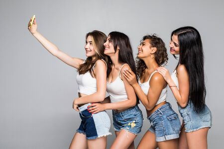 Happy smiling young four girls taking selfie on the phone isolated on white background.の写真素材