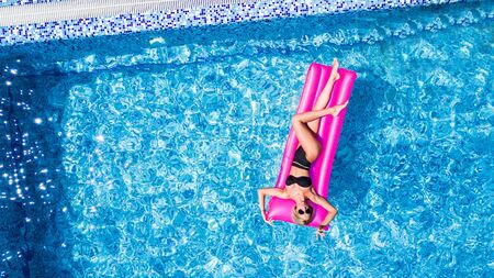 Sexy woman rest and sunbath on a float in the pool, top view aerial shot. Young woman in a bikini swimsuit floating on an inflatable pink mattress top viewの写真素材