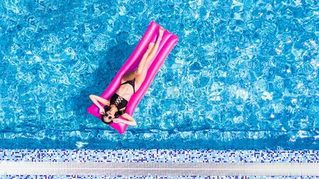Beautiful Young Woman sunbathing on inflatable pink mattress at swimming poolの写真素材
