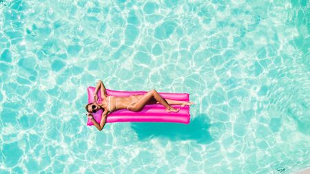 Attractive woman in bikini relaxes in the pool with a floating mattress