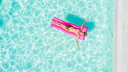 Sexy woman sunbath on a float in the pool, top view aerial shot. Young woman in a bikini swimsuit...