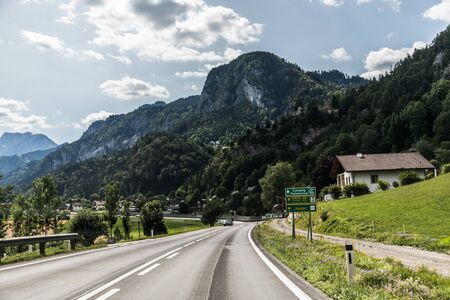 Autobahn or highway with a bridge in the mountains with clear marking surrounded by vibrant green trees under blue sky.の写真素材