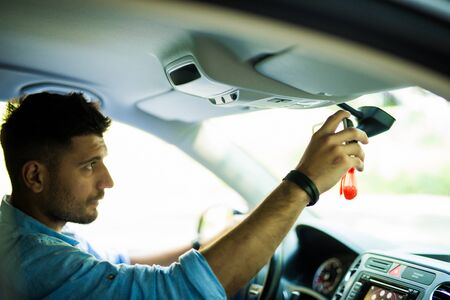 Man adjusting a rear view mirror while sitting in a car