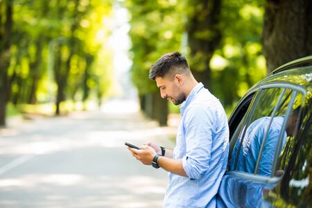 Successful man standing by his car texting on mobile phone