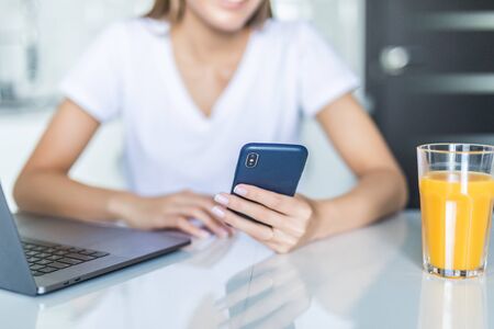 Pretty woman on the phone using laptop at home in the kitchenの写真素材