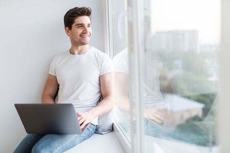 Man in headphones working on laptop and sitting on windowsillの写真素材