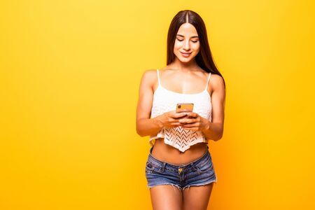 Photo of excited cheerful girlfriend browsing through her favorite page of some social media while isolated with yellow backgroundの写真素材